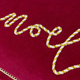 Close-up of Winter Noel Velvet Cotton Cushion in red, showing "Noel" script in cream and gold twisted cord rope appliqué on cotton velvet pile.