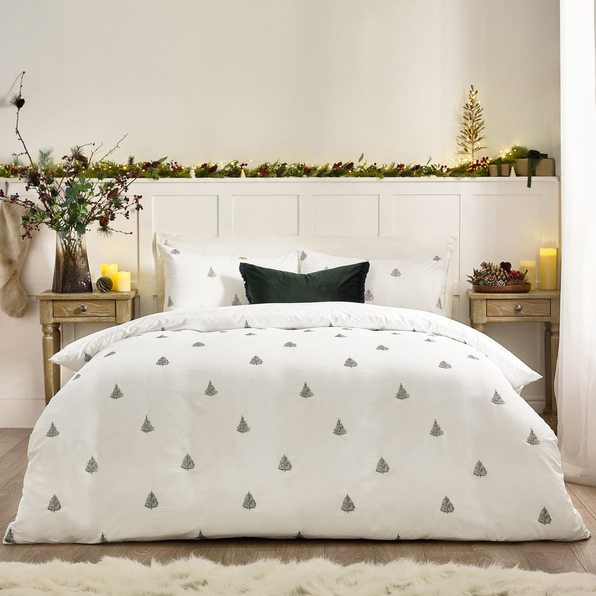 Winter Forest Woodland Duvet Cover Set in white cotton with embroidered green fir trees, dressed on a bed with matching pillowcases and a dark green cushion in a festive bedroom.