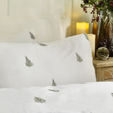 Winter Forest Woodland Duvet Cover Set in white cotton with embroidered green fir trees scattered across pillowcase and duvet, styled on a bed beside a candle-lit nightstand.