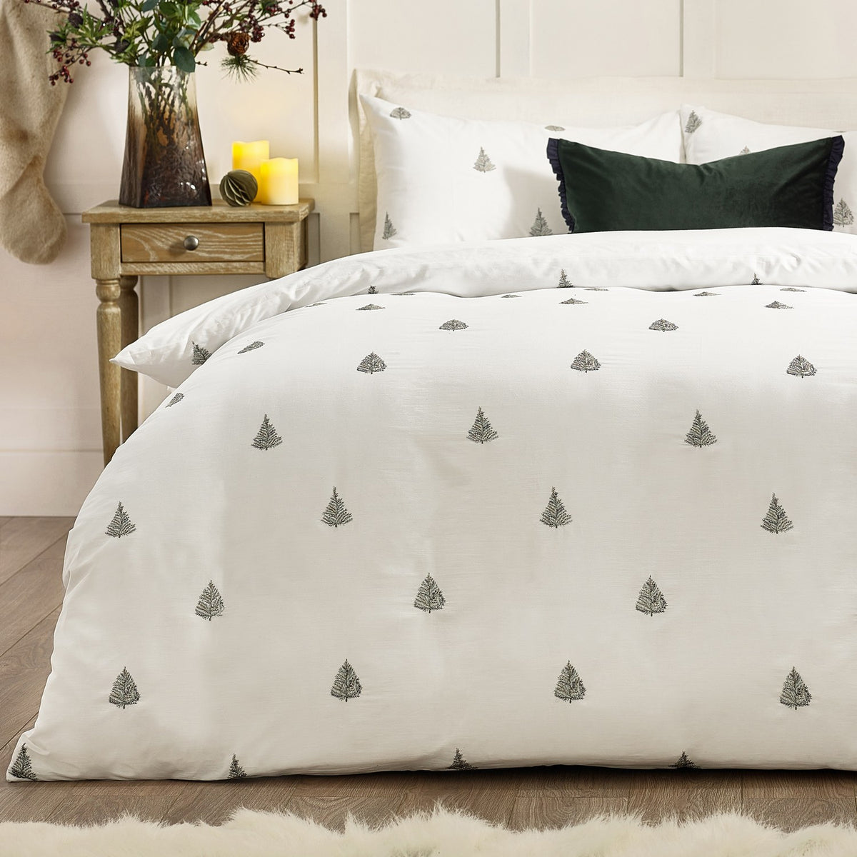 Winter Forest Woodland Duvet Cover Set in white cotton with embroidered forest green fir trees, styled on a bed with a dark green cushion in a bedroom setting.