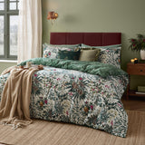 Cotton duvet cover set in Pine Green with cream leaf, pine cone and berry print, styled on a bed with a green reverse and cushions in a green bedroom.