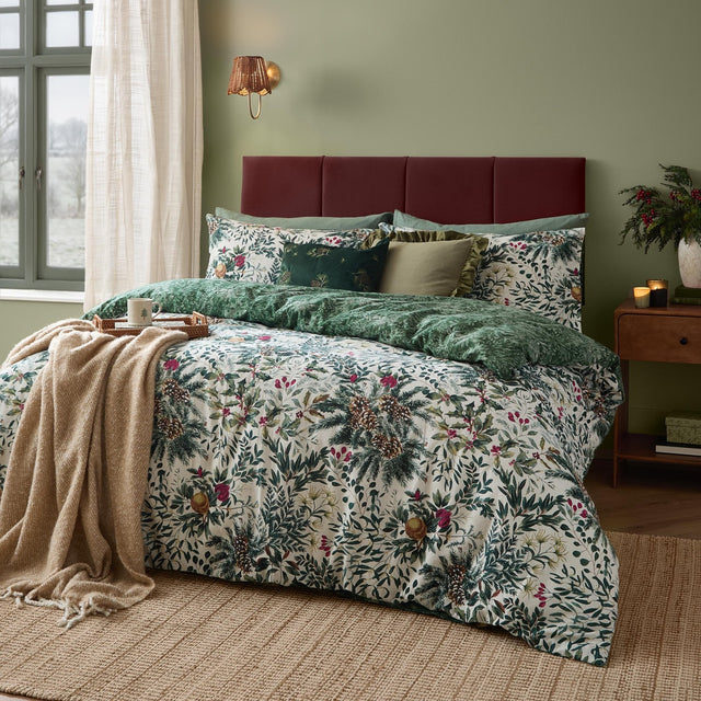 Cotton duvet cover set in Pine Green with cream leaf, pine cone and berry print, styled on a bed with a green reverse and cushions in a green bedroom.