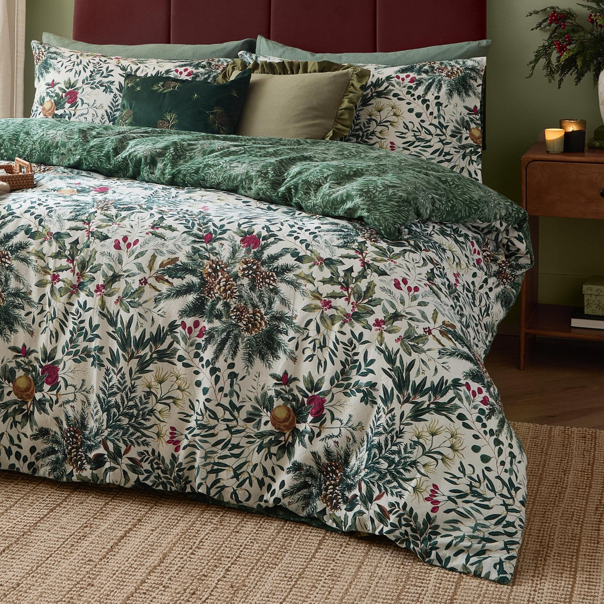 Winter Foliage Cotton Woodland Duvet Cover Set in Pine Green, cream cotton with leaf, pine cone and berry print, paired with a tonal green reverse, shown styled on a bed with cushions.