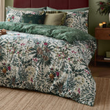 Winter Foliage Cotton Woodland Duvet Cover Set in Pine Green, cream cotton with leaf, pine cone and berry print, paired with a tonal green reverse, shown styled on a bed with cushions.