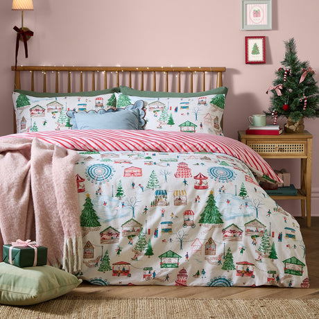 Winter Wonderland Cotton Striped Duvet Cover Set in Multi, shown on a bed with a festive fairground and market scene print, reversing to red and cream candy-cane stripes, styled in a pink bedroom.