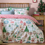 Winter Wonderland Cotton Striped Duvet Cover Set styled on a bed, showing the festive fairground print with matching pillowcases and red-and-cream striped reverse, in a pink bedroom setting.