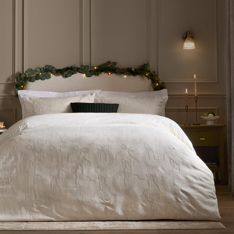 Winter Wreath Cotton Bows Duvet Cover Set in white on a bed, showing woven jacquard bows and wreaths in soft relief, styled in a bedroom with a green garland and lit candles.
