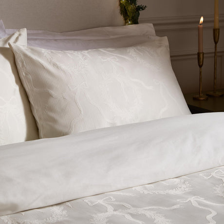Winter Wreath Cotton Bows Duvet Cover Set in white, styled on a bed with matching pillowcases featuring a woven jacquard bow and wreath pattern, beside lit candles in a bedroom setting.