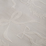 Close-up of the Winter Wreath Duvet Cover Set showing a woven jacquard pattern of bows, ribbons and wreaths in raised relief on a cream-white ground.
