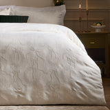 Winter Wreath Cotton Bows Duvet Cover Set in white, shown on a bedroom bed with textured jacquard bows and wreath detailing, styled with candles and a dark green cushion.
