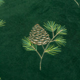 Close-up of the Winter Pines cushion in spruce green velvet, showing an embroidered pine cone and needled branch design in green and gold threads.