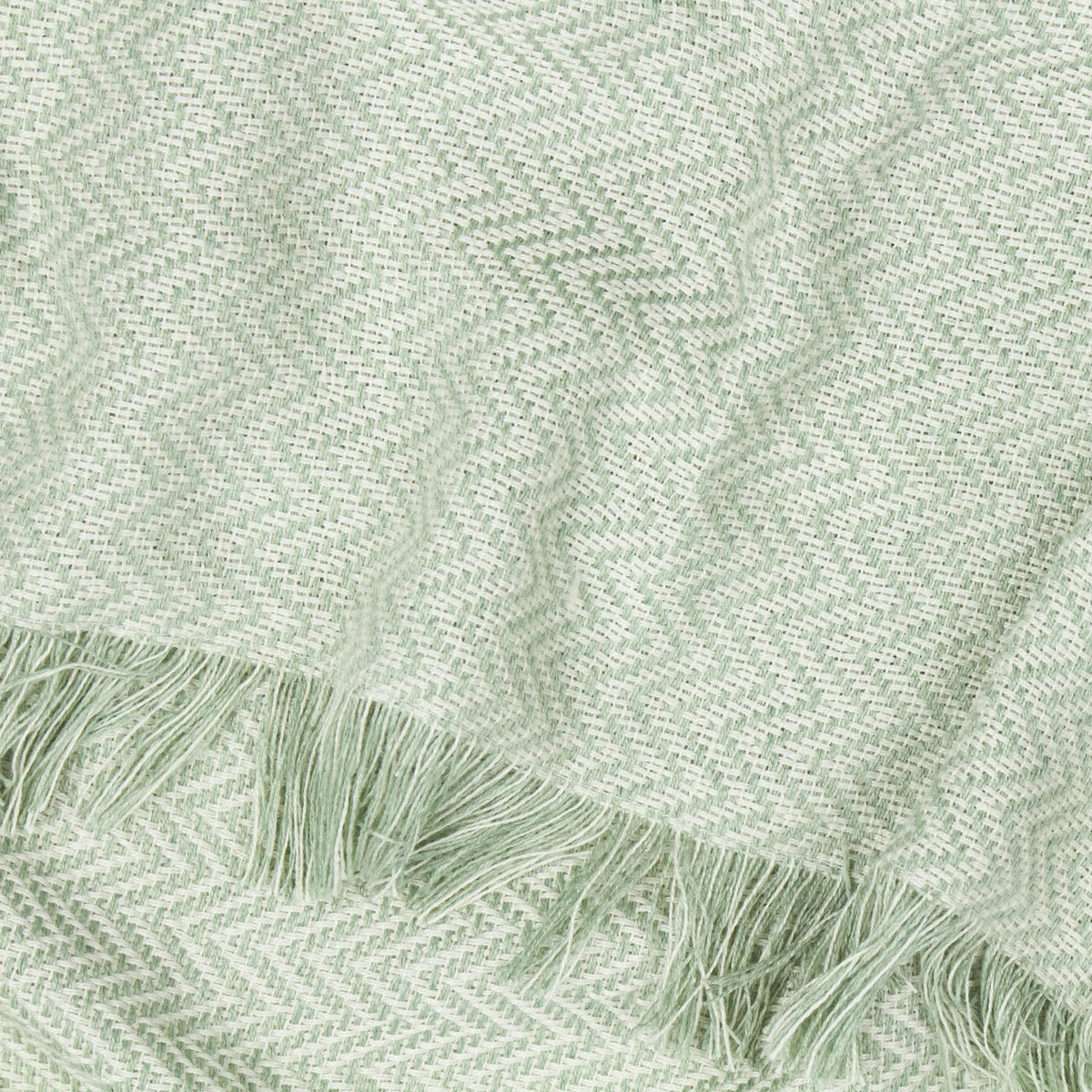 Wisley Herringbone Polyester Throw in leaf green, close-up of chevron weave texture with cream detailing and knotted tasselled fringe edge.