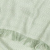 Wisley Herringbone Polyester Throw in leaf green, close-up of chevron weave texture with cream detailing and knotted tasselled fringe edge.