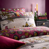 Reversible duvet cover set in a multicolor Halloween print with skulls, spell books and cobwebs on one side and a pink oval pattern on the reverse, shown on a bed in a pink-toned bedroom with candles.