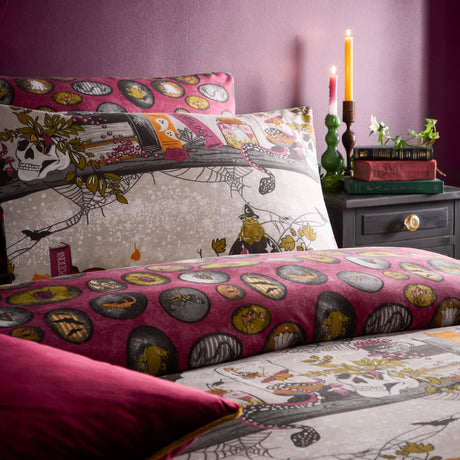 Reversible duvet cover set in a multicolor Halloween print with skulls, spell books and cobwebs on one side and a pink oval pattern on the reverse, shown on a bed in a pink-toned bedroom with candles.