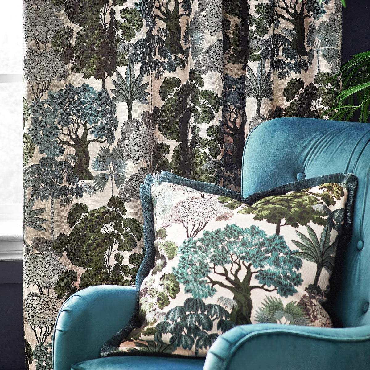 Green Woodlands Jacquard fully lined eyelet curtains, pleated in a living room, featuring a woven woodland scene in green, teal and grey on cream, with a matching cushion on a teal armchair.