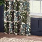 Woodlands Jacquard Fully Lined Eyelet Curtains in green, showing a woven woodland scene of trees and palms on cream fabric, hung by a window in a room with navy panelling.