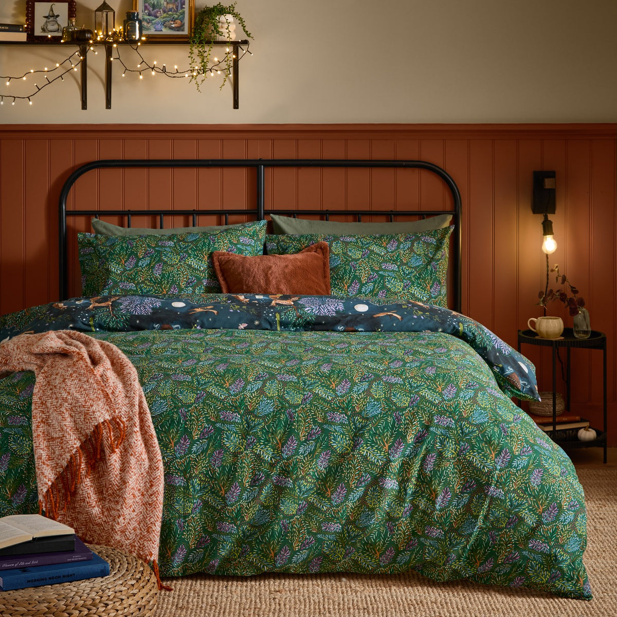 Woodland Ritual reversible duvet cover set on a bed, showing the green foliage side with navy woodland-print pillowcases, styled in a bedroom with a rust-toned throw.