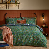 Woodland Ritual reversible duvet cover set on a bed, showing the green foliage side with navy woodland-print pillowcases, styled in a bedroom with a rust-toned throw.