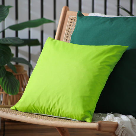 Plain Printed Polyester Cushion in lime green, square 43 x 43cm design, shown on a rattan chair with a dark teal cushion behind it in an outdoor setting.