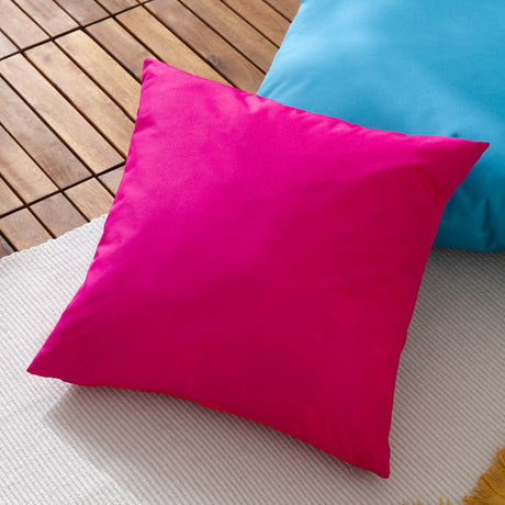 Plain Printed Polyester Cushion in bright pink, square 43 x 43cm outdoor cushion shown on a wooden deck beside a blue cushion.