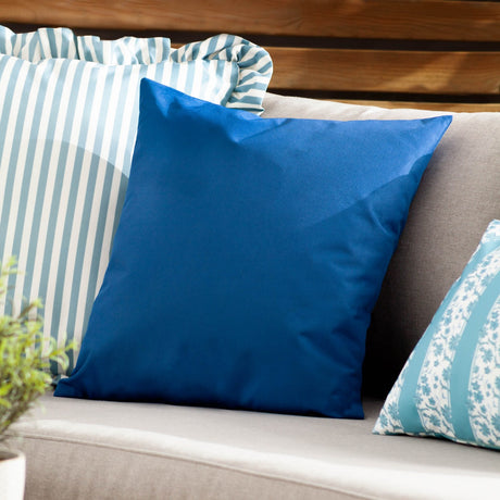 Plain Printed Polyester Cushion in royal blue on an outdoor sofa, shown beside striped and floral patterned cushions on a garden bench.