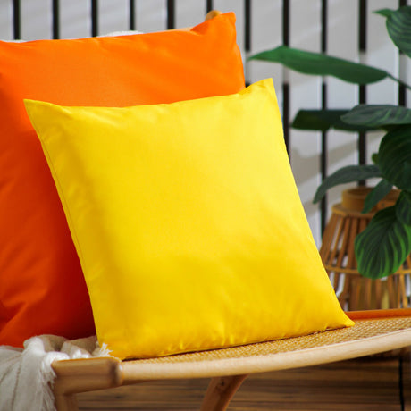 Square yellow polyester outdoor cushion with plain finish, shown against an orange cushion on a rattan chair in a garden setting.