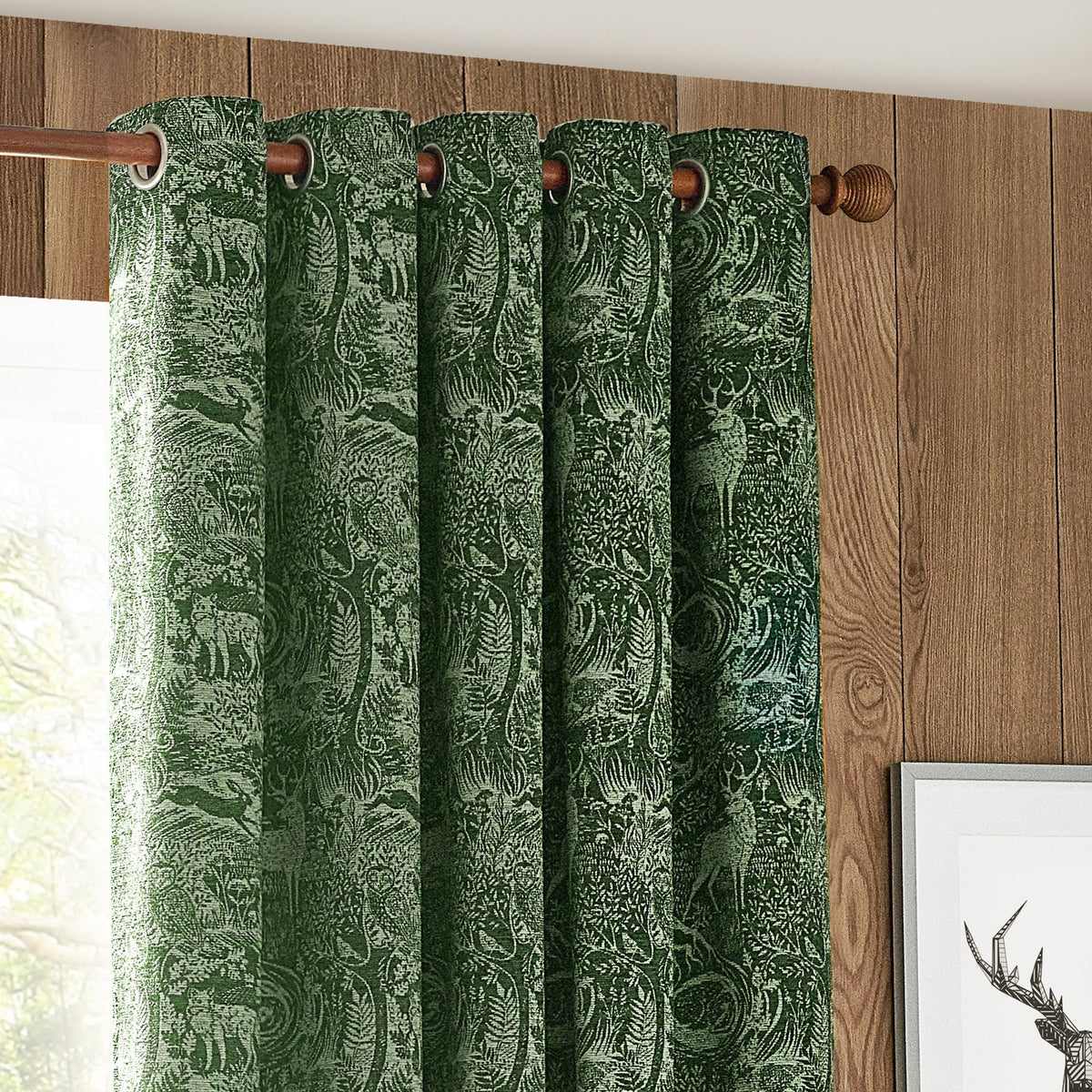 Winter Woods Chenille Lined Eyelet Curtains in emerald, showing woodland deer and forest jacquard fabric with eyelet header on a wooden curtain pole.