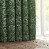 Winter Woods Chenille Lined Eyelet Curtains in emerald, showing folded panels with a tonal woodland motif of deer and birds, hung beside a window in a room setting.