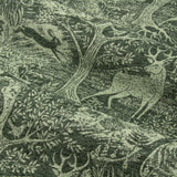 Close-up of Winter Woods eyelet curtain fabric in emerald, showing a chenille jacquard woodland design with deer, hares, birds and trees woven in tonal green.