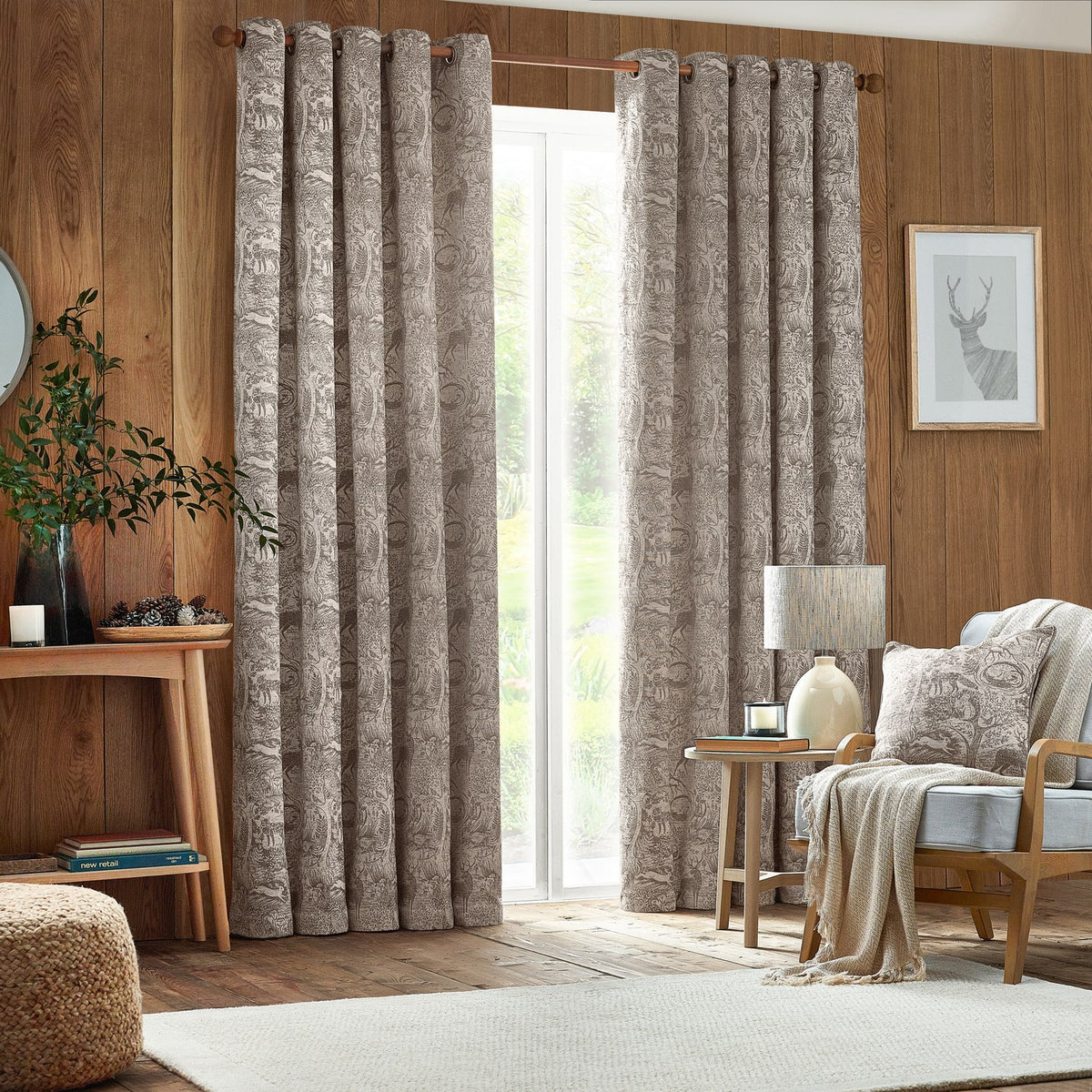 Winter Woods Chenille Lined Eyelet Curtains in taupe with woven woodland animal jacquard pattern, hung on a wooden pole beside a bright window in a living room.
