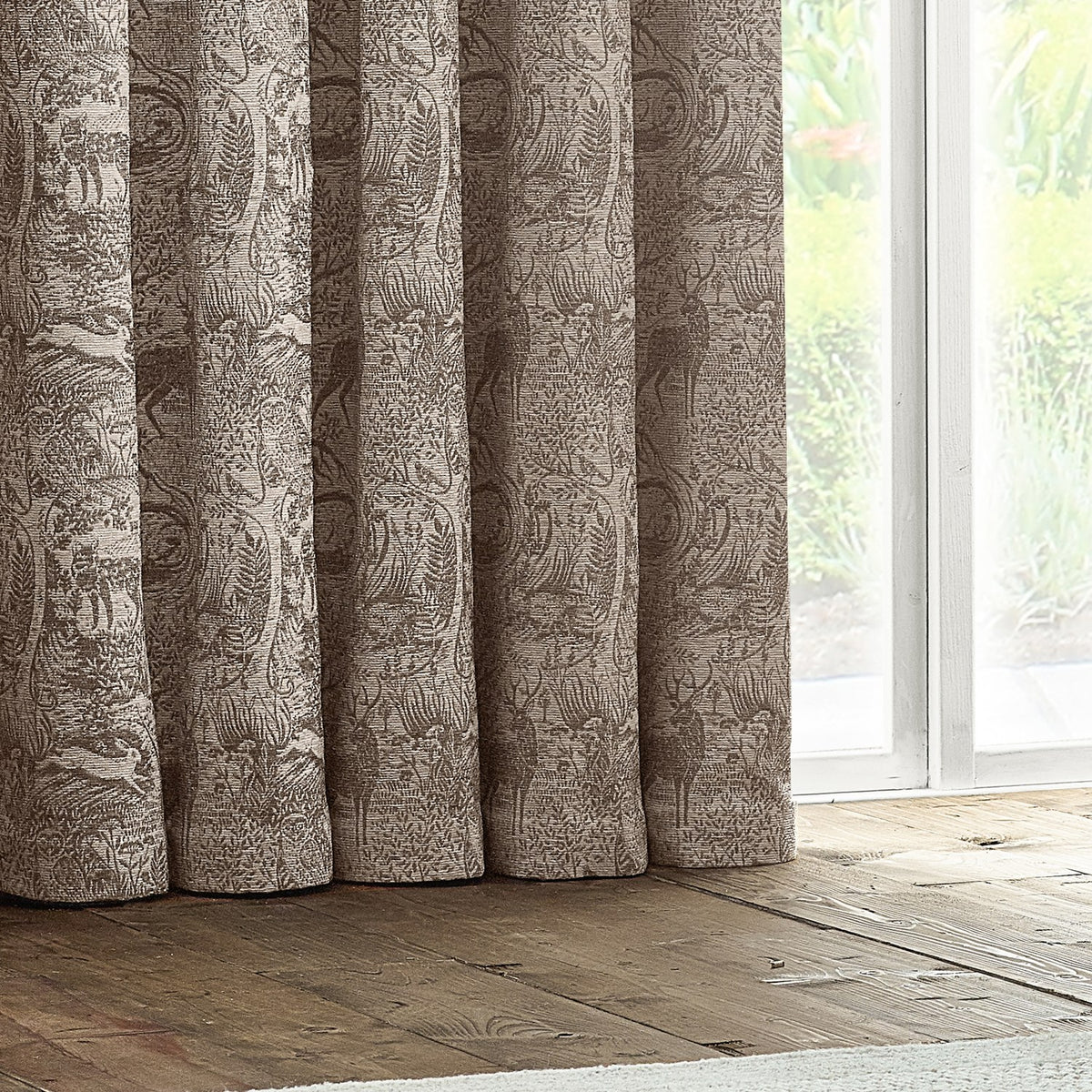 Winter Woods Chenille Lined Eyelet Curtains in taupe, showing a woven woodland animal and tree pattern in soft folds beside a bright window.