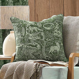 Winter Woods Jacquard Chenille Cushion in emerald, woven with a woodland scene of deer, hare, squirrel and trees, shown on an armchair with a beige waffle throw.