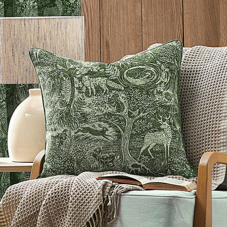Winter Woods Jacquard Chenille Cushion in emerald, woven with a woodland scene of deer, hare, squirrel and trees, shown on an armchair with a beige waffle throw.