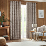Taupe Winter Woods jacquard chenille cushion with woodland stag and hare motif, styled on a light armchair beside patterned curtains in a wood-panelled living room.