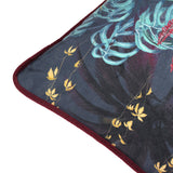 Close-up corner view of the Zinara Animal Velvet Cushion in black, showing teal leaf print, gold trailing blooms and wine-red velvet piping on a dark background.