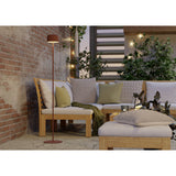 Roccanova-L solar LED floor lamp in terracotta steel with a drum-shaped head and round disc base, shown beside an outdoor corner sofa with cushions.