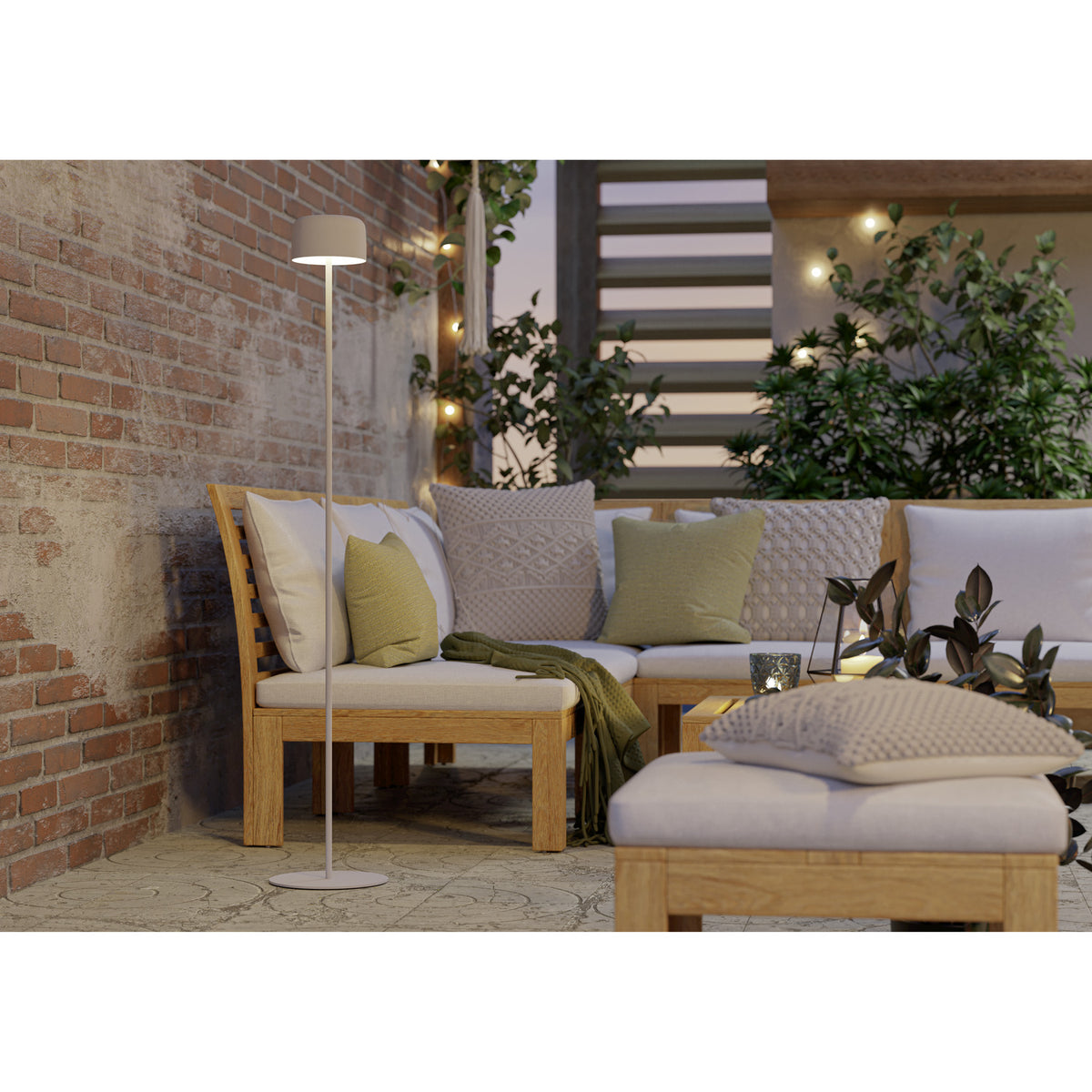 Roccanova-L solar LED floor lamp in white with drum-shaped head, slim steel stem and round base, shown beside an outdoor corner sofa with cushions on a patio.