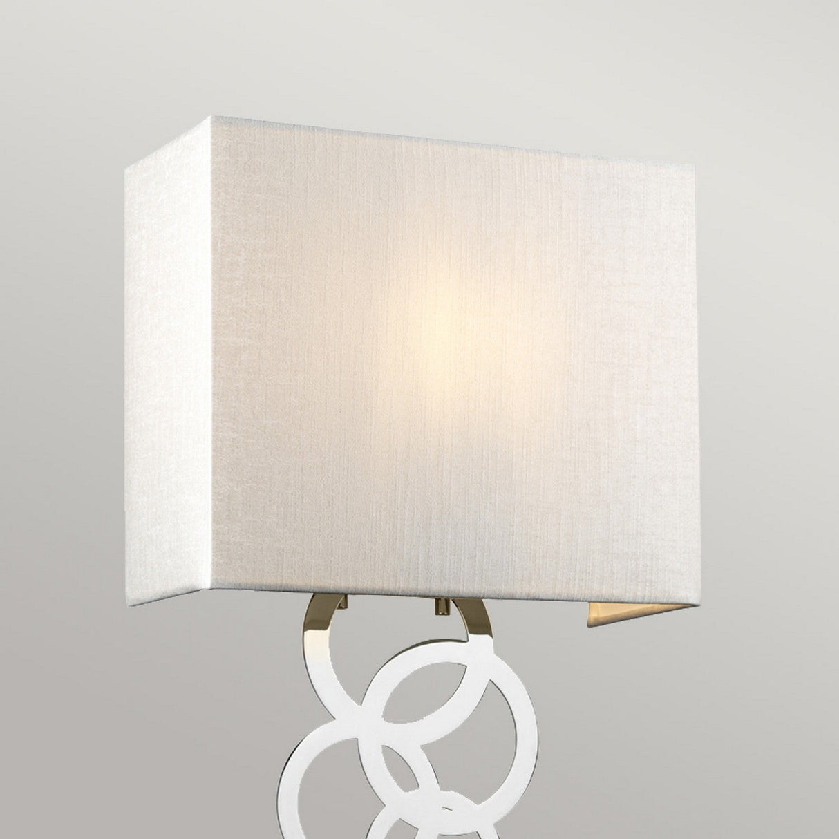 Introducing the Rosa Medium 1 Light Wall Light - Polished Chrome: a contemporary wall sconce with a rectangular fabric lampshade and a base adorned with polished chrome interlocking circles. This sophisticated wall light gently emits a soft, warm glow against any plain background.