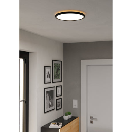 Rovito LED Flush Ceiling Light 30cm in black, round black ring with white diffuser mounted on a hallway ceiling above framed wall art and a sideboard.