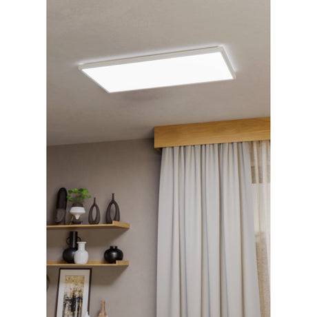 Rovito LED Panel Light, rectangular white ceiling fixture with integrated LED and plastic diffuser, shown mounted on a living room ceiling above curtains and shelving.