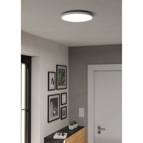Rovito Smart Colour Changing LED Flush Ceiling Light, 30cm round white plastic fixture with opal diffuser, shown mounted in a hallway ceiling above framed wall art.