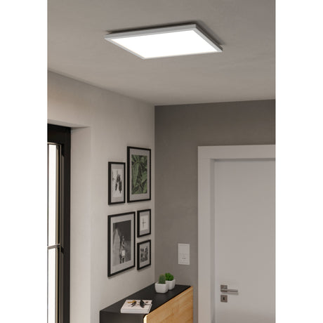 Rovito Smart Colour Changing LED Panel Light, 39 x 39cm square white ceiling fixture, shown recessed-style on a hallway ceiling above framed artwork and a sideboard.