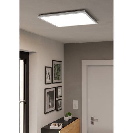 Rovito Smart LED Panel Light, a square white ceiling fixture with a slim frame, shown illuminated in a hallway above framed wall art and a sideboard.