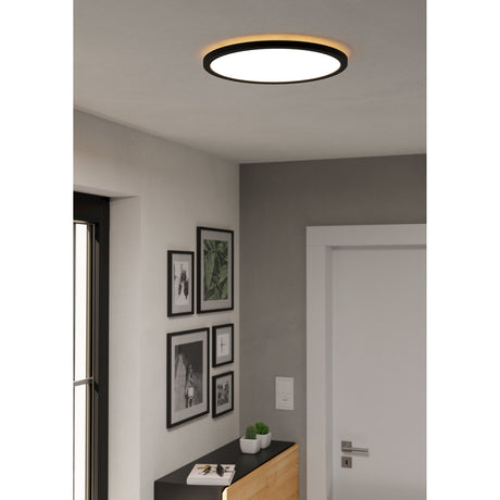 Rovito Smart LED Flush Ceiling Light 38.9cm in black, round design with white diffuser and warm backlit edge, shown mounted on a hallway ceiling above a gallery wall of framed prints.