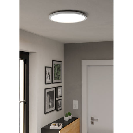 Rovito Smart LED Flush Ceiling Light 38.9cm in white, round plastic body with glowing shade, shown mounted in a hallway ceiling near framed artwork.