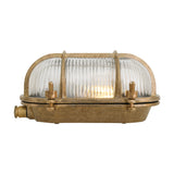 Ruben Small Bulkhead wall light in brass with oval body, cage bars over clear ribbed glass, and side cable entry, shown on a plain white background.