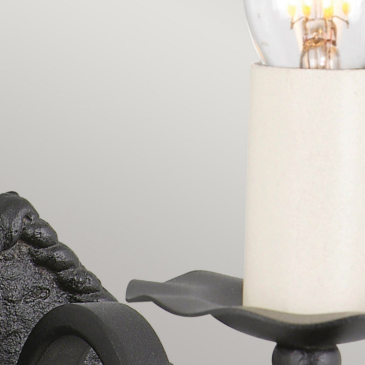 Close-up of the Rectory 1 Light Small Wall Light in black, inspired by medieval decor with a partially visible candle-shaped light bulb on a beige holder. The light gray background enhances its rustic interior appeal.