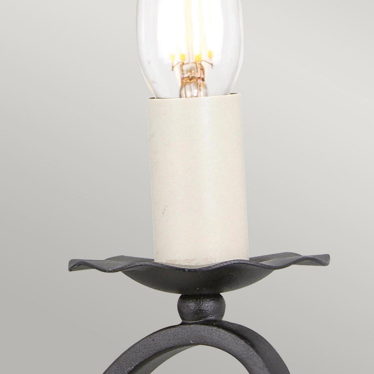 Close-up of the Rectory 2 Light Small Wall Light in black, featuring vintage-style bulbs reminiscent of candle designs, elegantly housed in a wrought iron frame with scalloped edges. The soft gray background highlights the simplicity and elegance of this ideal piece for rustic interiors.