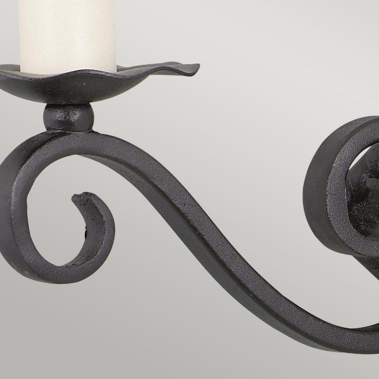 A detailed view of the Rectory 2 Light Small Wall Light in black showcases its elegant scrollwork design. The piece, featuring a medieval-inspired aesthetic with space for a single unlit white candle above a circular base, is striking against the plain light gray background.